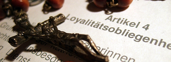 Kreuz und Rosenkranz, auf dem Text des Artikels 4 über die Loyalitätsobliegenheiten für eine Anstellung in der katholischen Kirche liegend